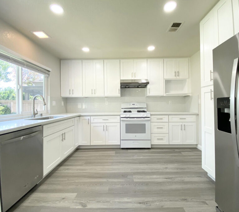 White kitchen with wood floors and sliver appliances.
